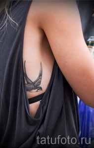 Фотография минималистичной татуировки ласточки, выполненной в технике blackwork, на женском боку.
