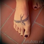Фото тату ласточки на стопе. Черно-серая татуировка с тонкими линиями и детальной проработкой.
