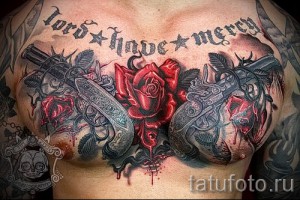 Фото тату на мужской груди с изображением пистолетов, красных роз и надписи 'Lord Have Mercy'. Детализированный рисунок в стиле реализм.