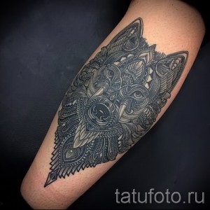 Черно-серая татуировка волка в стиле геометрии на икре. Детализированный рисунок с множеством мелких элементов и узоров.