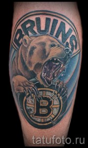 Фото тату медведя в круге с надписью Bruins на предплечье. Реалистичный рисунок татуировки с использованием коричневых, черных и белых оттенков.