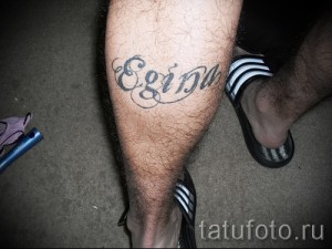 Фото тату на голени с именем "Egina", выполненным в каллиграфическом стиле. Черно-серый оттенок, плавные линии и элегантный дизайн.