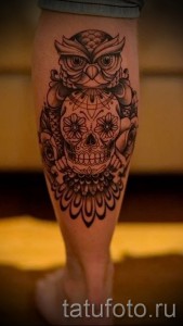 Фото тату совы, стилизованной под сахарный череп (sugar skull) на голени. Черно-белый рисунок с детальной проработкой.