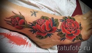 Фото тату на стопе: три классические розы с листьями, выполненные в традиционном стиле с яркими цветами.