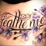Фото тату надписи 'Breathe me' с изображением фиолетовых цветов на боку. Элегантный шрифт и яркие краски.
