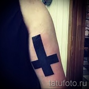 Фото тату черного перевернутого креста на предплечье. Минималистичный и стильный рисунок татуировки.