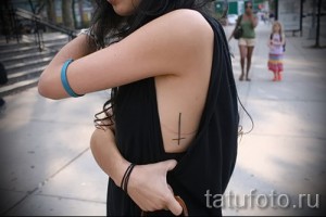 Фото тату на боку с изображением перевернутого креста. Простой, но вызывающий рисунок.