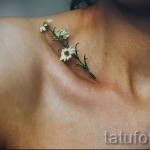 Фото татуировки с изображением маленьких белых цветов, расположенных на ключице. Минималистичный дизайн с реалистичными деталями.