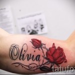 Фото татуировки: надпись "Olivia" с изображением красной и бутона розы на руке, выполненная в акварельном стиле.