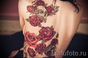 Фото тату на спине с изображением черепа, увитого красными розами. Детализированный рисунок татуировки выполнен в реалистичном стиле.