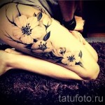 Фото тату цветущей сакуры на колене. Нежные розовые цветы с детально проработанными лепестками и черными стеблями, выполненные в реалистичном стиле.