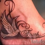 Фото тату: татуировка белого голубя с расправленными крыльями и надписью 'Faith' на лодыжке. Эскиз выполнен в черно-белой гамме с использованием теней.