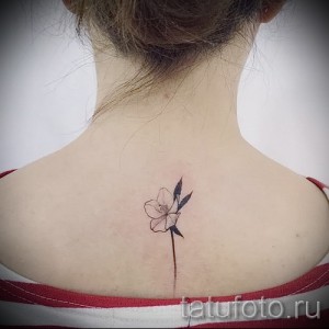 Фото тату: нежный цветок с тонкими лепестками, выполненный в минималистичном стиле, расположен на задней части шеи девушки.