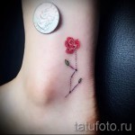 Фото тату с изображением маленькой красной розы на лодыжке. Рисунок выполнен в минималистичном стиле с использованием тонких линий и точечных элементов.
