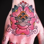 Фото татуировки на руке: розовая роза с бабочкой в стиле олд скул, яркие цвета и четкие контуры.