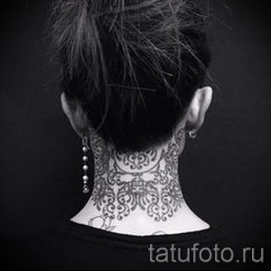 Фото тату: изящный черный орнамент, покрывающий заднюю часть шеи женщины. Детализированный рисунок татуировки выполнен в стиле ориентал с элементами геометрии.