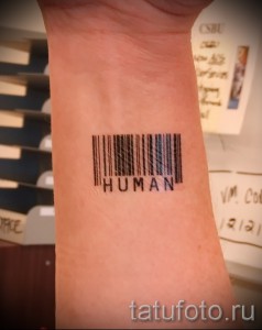 Фото тату штрихкода с надписью 'HUMAN' на запястье. Черно-белый минималистичный рисунок татуировки, подчеркивающий человеческую сущность.