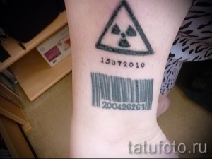 Фото тату штрих-кода и знака радиации на запястье. Черно-белый рисунок татуировки, минималистичный стиль, расположен на внутренней стороне запястья.
