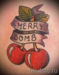 Фото тату: две вишни с надписью "Cherry Bomb" на ленте, выполненные в стиле олд скул с использованием ярких цветов и четких контуров.