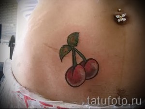 Фото тату вишни на животе. Небольшой рисунок с двумя красными ягодами и зелеными листьями. Идеальный эскиз для девушек.