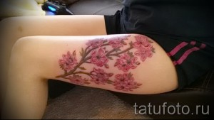Фото тату цветущей сакуры на бедре. Красивый рисунок с розовыми цветами и ветками. Элегантный эскиз для девушек.