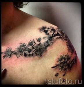 Фото тату на плече: ветка цветущей сакуры, выполненная в технике blackwork. Изящный рисунок татуировки с детально проработанными лепестками и ветвями.