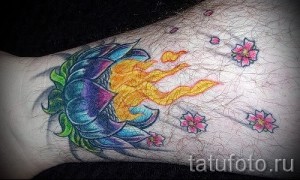 Фото тату цветущего лотоса, из которого вырывается пламя, с летящими розовыми лепестками. Рисунок выполнен в ярких цветах с использованием черных контуров.