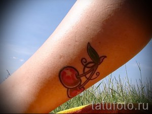 Фото тату двух вишен с зеленым листком и завитками на руке. Элегантный, минималистичный рисунок татуировки.