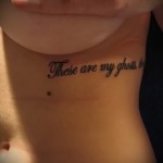 Фото тату надписи 'These are my ghosts' черным цветом, выполненной каллиграфическим шрифтом на боку женщины.