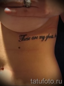 Фото тату надписи 'These are my ghosts' черным цветом, выполненной каллиграфическим шрифтом на боку женщины.