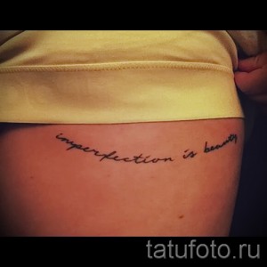 Фото минималистичной тату надписи 'imperfection is beauty' черным цветом, расположенной на боку.