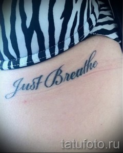 Фото тату надписи 'Just Breathe' черным цветом, выполненной каллиграфическим шрифтом на внутренней стороне предплечья женщины.