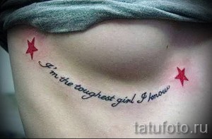 Фото тату: небольшая текстовая татуировка с надписью 'I’m the toughest girl I know' и двумя красными звездами, расположенная под грудью. Черный шрифт.