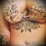 Фото тату: стилизованный лотос в технике дотворк, выполненный между грудью женщины. Детализированный рисунок татуировки с использованием черных чернил.