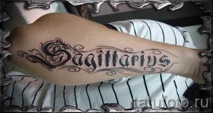 Фото татуировки с надписью 'Sagittarius' на руке, выполненной в каллиграфическом стиле с декоративными элементами.
