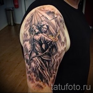 Фото тату Артемиды на плече, выполненное в реалистичном стиле с использованием черно-серых оттенков и эффекта облаков.