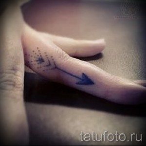 Маленькая татуировка стрелы на пальце руки, выполненная в технике дотворк, с использованием точек и тонких линий.