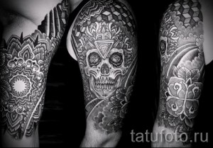 Фото тату на руке: рукав, выполненный в технике dotwork, с изображением черепа в центре мандалы и окруженного геометрическими узорами. Детализированный рисунок татуировки в черном цвете.