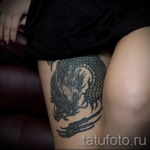 Фото тату: монохромный рисунок дракона на бедре, выполненный в технике blackwork, с акцентом на детализацию чешуи и выразительный взгляд.