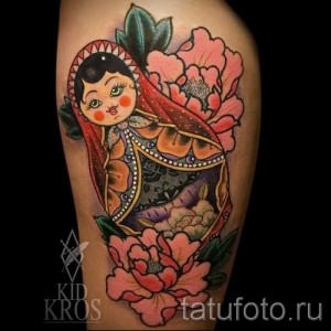 Фото тату: Красочная татуировка матрешки, окруженной розовыми пионами, на руке женщины.