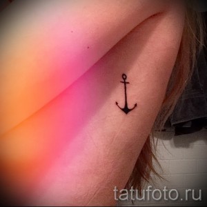 Фото тату маленького черного якоря на женской лопатке. Простой и лаконичный рисунок татуировки, выполненный в технике лайна.