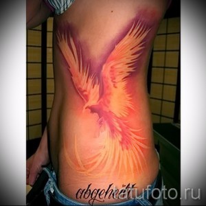 Фото акварельной татуировки феникса на женском боку. Нежные переходы цветов и размытые контуры создают эффект живописи на коже.
