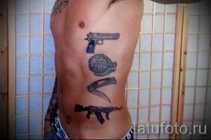 Фото тату на боку с изображением пистолета, гранаты, ножа и надписи LOVE. Черно-белый рисунок, смелый дизайн, мужская татуировка.