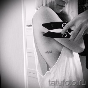 Фото тату надписи на греческом языке на женском боку. Черно-белый рисунок татуировки, выполненный в минималистичном стиле.