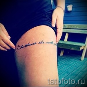 Фото тату: надпись 'She believed she could, so she did' на бедре, выполненная черными чернилами. Текст расположен вдоль линии бедра.