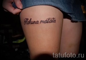 Фото тату: надпись 'Hakuna Matata' на внутренней стороне бедра, выполненная черными чернилами. Текст расположен горизонтально, вдоль линии бедра.