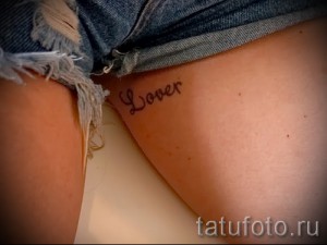 Фото тату надписи "Lover" на бедре, выполненное простым шрифтом. Минималистичный рисунок татуировки.