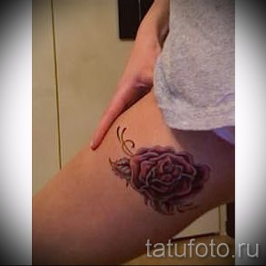 Фото тату розы на бедре, выполненное в реалистичном стиле с использованием красных и зеленых оттенков. Детализированный рисунок татуировки.