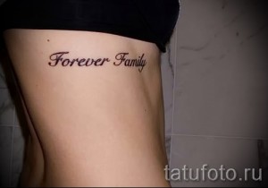 Фото тату надписи 'Forever Family' на боку, выполненное в каллиграфическом стиле. Идеальный эскиз тату для тех, кто ценит семью и близких.