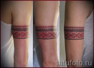 Фото тату браслета на руке, выполненного в стиле традиционной народной вышивки. Красные и белые узоры на черном фоне создают эффектный контраст.